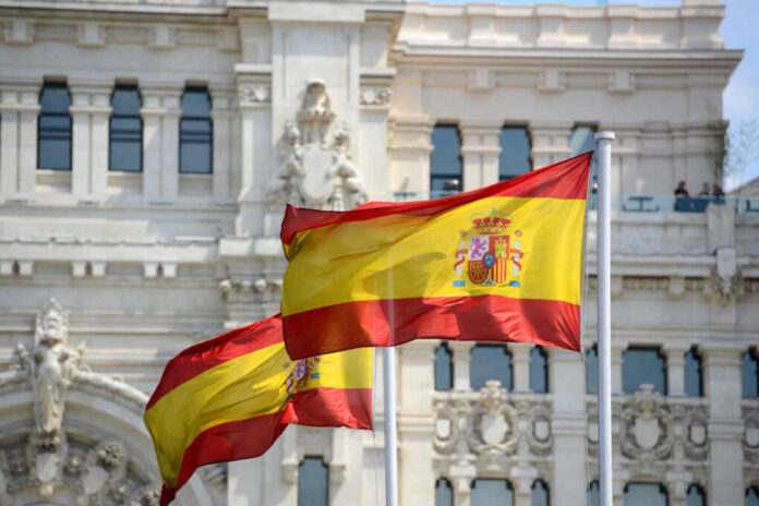 Flag,Of,Spain,In,The,Wind,In,Front,Of,Palace