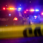 Police cars with flashing lights at a nighttime scene behind crime scene tape