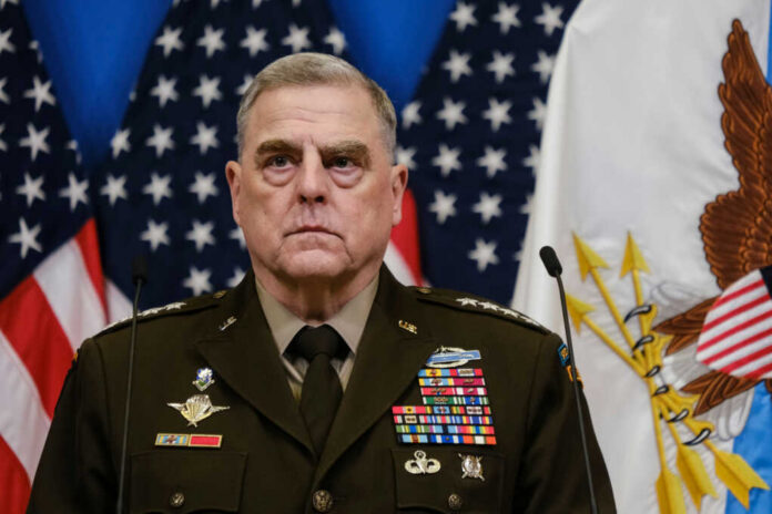 A military leader in a decorated uniform standing in front of U.S. flags