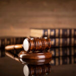 A wooden gavel resting on a round base with law books in the background