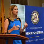 Female politician delivering a speech at a podium with a banner behind her