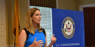 Female politician delivering a speech at a podium with a banner behind her