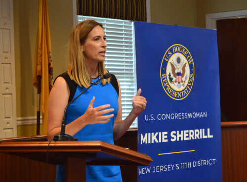 Female politician delivering a speech at a podium with a banner behind her