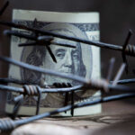 A rolled hundred dollar bill partially obscured by barbed wire