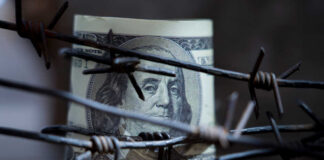 A rolled hundred dollar bill partially obscured by barbed wire