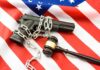 A handgun chained and placed on an American flag with a gavel nearby