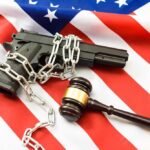A handgun chained and placed on an American flag with a gavel nearby