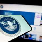 Close-up of a mobile device displaying the TSA logo with a blurred background of a website