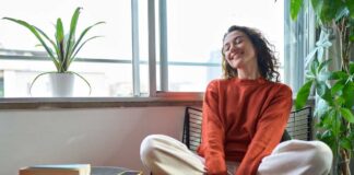 A relaxed woman sitting in a chair with a smile, surrounded by plants and natural light