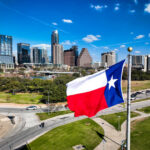 Texas flag waving in front of the Austin skyline under a clear blue sky