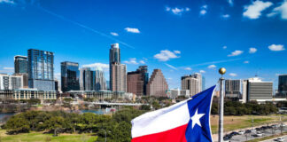 Texas flag waving in front of the Austin skyline under a clear blue sky