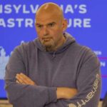 Man in a hoodie with arms crossed, looking serious in front of a presentation background