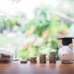 A piggy bank wearing a graduation cap next to stacks of coins