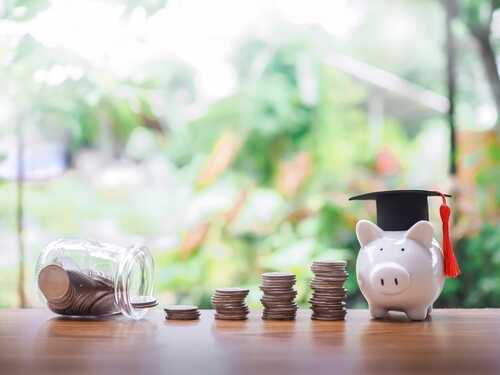 A piggy bank wearing a graduation cap next to stacks of coins