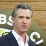 A man in a suit speaking at an outdoor event with a microphone