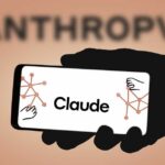 A hand holding a smartphone displaying the name 'Claude' with abstract graphics