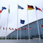 Flags of various countries in front of a modern building under a cloudy sky