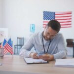A man in an office setting surrounded by American flags, reviewing documents
