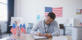 A man in an office setting surrounded by American flags, reviewing documents