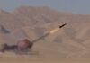 A missile launching into the sky with smoke and flames in a desert setting