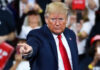 A man in a blue suit and red tie gestures while speaking at a rally