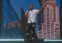 A speaker on stage holding a microphone with a city skyline in the background