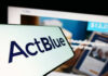 Close-up of ActBlue logo on a mobile device with a website in the background