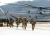 Marines in combat gear walking towards a helicopter