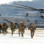 Marines in combat gear walking towards a helicopter