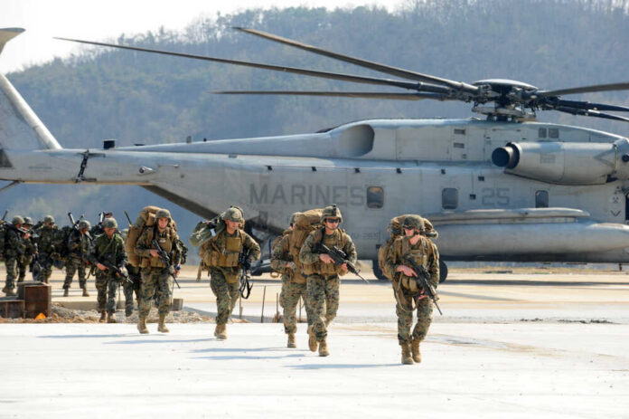 Marines in combat gear walking towards a helicopter