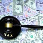 MASSIVE Gap Revealed: NYC’s Financial Black Hole A gavel with the word 'TAX' on it placed on a background of US dollar bills