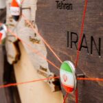 Close-up of a wooden map highlighting Iran with travel pins and red strings
