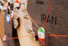 Close-up of a wooden map highlighting Iran with travel pins and red strings