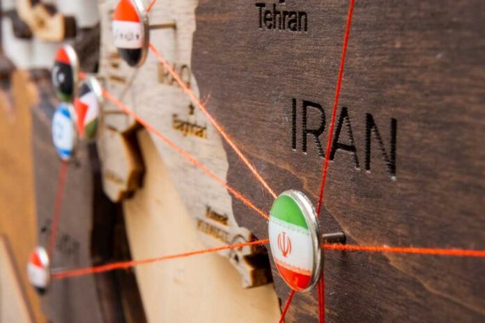 Close-up of a wooden map highlighting Iran with travel pins and red strings