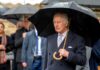 A man in formal attire holding an umbrella in the rain