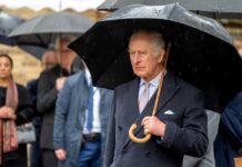 A man in formal attire holding an umbrella in the rain