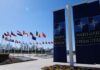 Flags of various nations displayed outside NATO headquarters under a clear blue sky