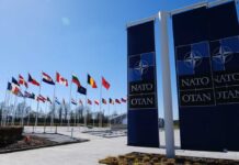 Flags of various nations displayed outside NATO headquarters under a clear blue sky