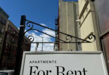 Sign indicating apartments available for rent against a blue sky