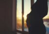 Silhouette of a pregnant woman standing by a window at sunset