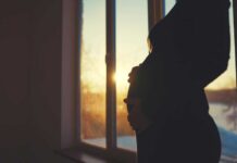 Silhouette of a pregnant woman standing by a window at sunset