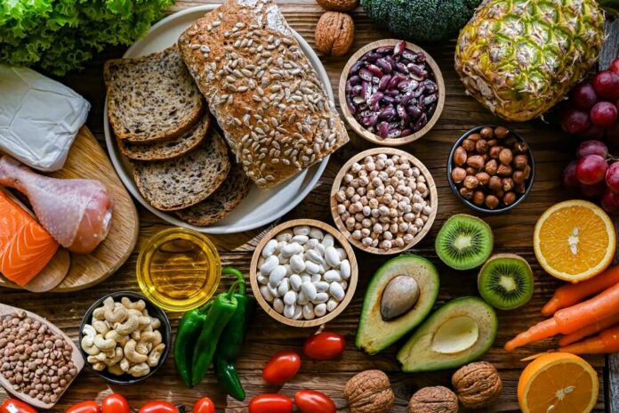 A variety of fresh foods including vegetables, fruits, grains, and proteins arranged on a wooden surface