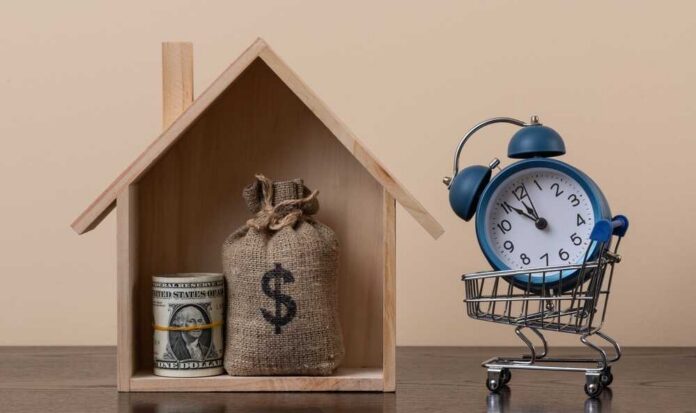 A wooden house model with money and a clock in a shopping cart