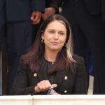 A woman in a black blazer sitting outdoors, holding a water bottle