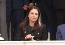 A woman in a black blazer sitting outdoors, holding a water bottle