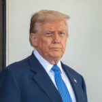 A man in a suit with a serious expression standing outdoors
