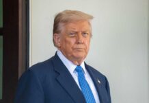 A man in a suit with a serious expression standing outdoors