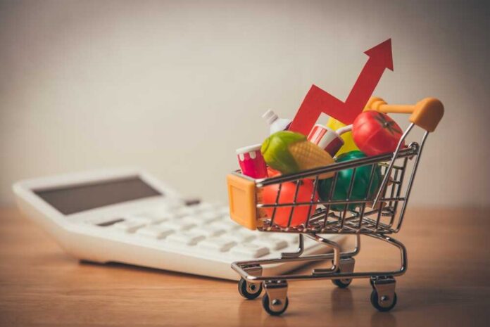 shutterstock_2664520873.jpg A shopping cart filled with colorful grocery items next to a calculator and an upward trend arrow
