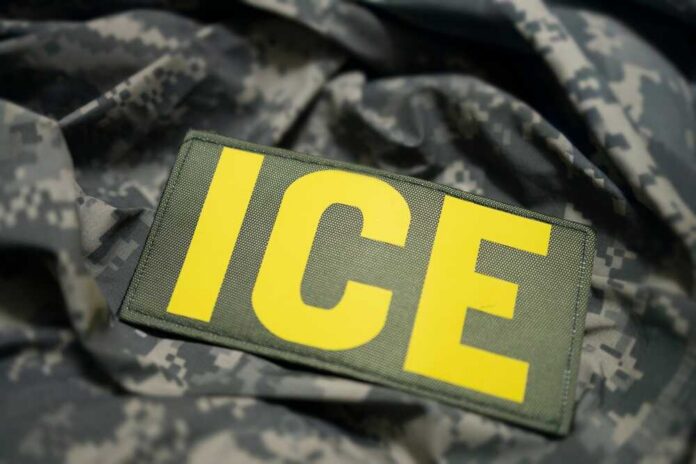 shutterstock_2700484957.jpg Close-up of a military patch with the letters ICE on a camouflage background