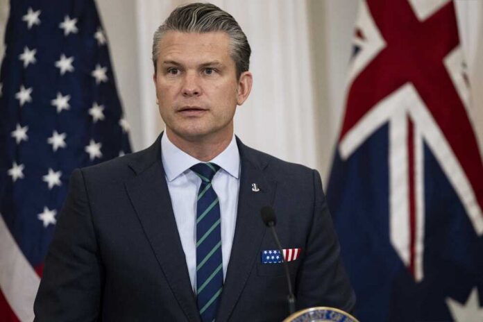 A man in a suit speaking at a podium with flags in the background
